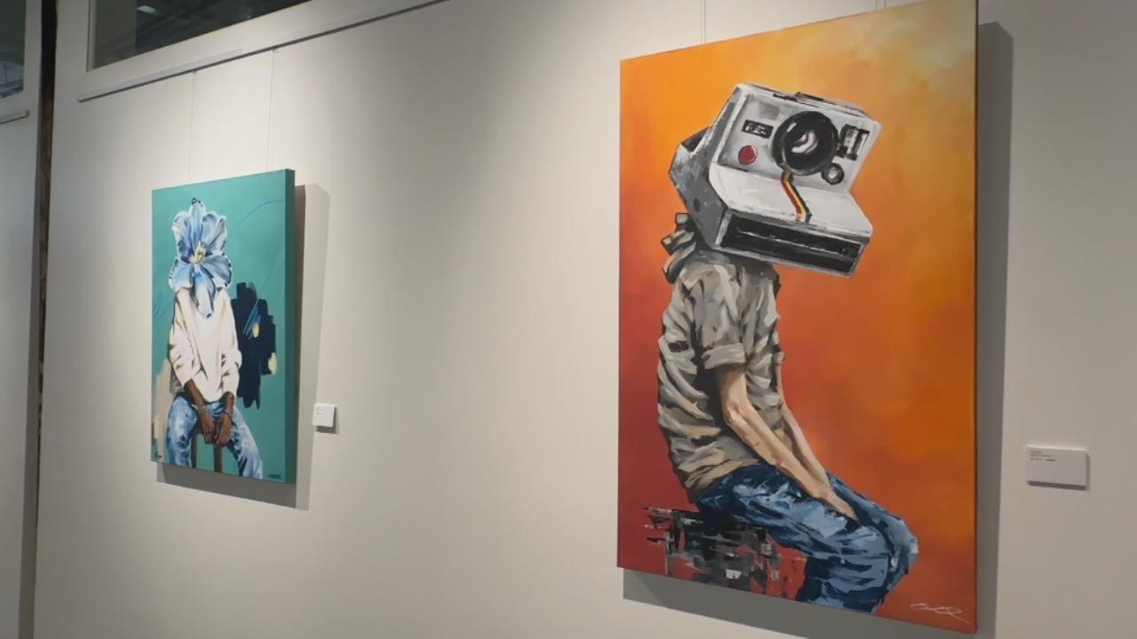 Randolph Read painting of a seated figure with a Polaroid camera for a head on an orange background, exhibited at WOMPA